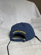 Gorra de béisbol azul marino con visera curva y bordado frontal en amarillo que dice "LOVE & PEACE" y debajo "PP:ONE".