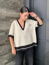 Sweater color crema con cuello en V y ribetes negros en cuello, puños y ruedo.