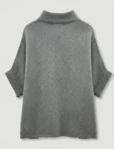 Capa o poncho tejido color verde esmeralda, con cuello polera alto que se cierra con un botón grande en el lateral. Presenta mangas cortas estilo japonesa y un calce amplio.