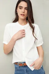 Camisa blanca de manga corta abullonada, cuello mao y botones forrados.