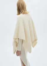 Poncho de punto color crudo, con cuello redondo y bajo asimétrico. Tejido con lana, poliéster y acrílico.