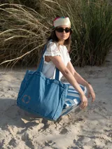 Bolso tote de denim color celeste con asas de hombro y logo bordado en color naranja.