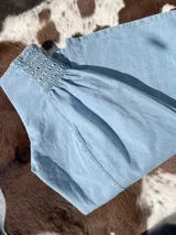 Pantalón de denim celeste claro, con cintura alta fruncida con elástico (smock) y dos botones decorativos en el lateral superior. El tejido es de algodón 100%.