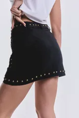 Minifalda negra de gamuza con tachas doradas y cierre metálico en el lateral.