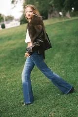 Jeans de denim azul oscuro con efecto lavado y desgaste sutil en la parte delantera de los muslos y las rodillas. Diseño de tiro alto, cinco bolsillos y corte acampanado desde la rodilla hacia el bajo.