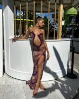 Vestido largo de corte ajustado, con estampado abstracto en tonos rosados y marrones. Presenta un escote pronunciado con detalle de volados en color púrpura, abertura en el abdomen y tajo lateral.