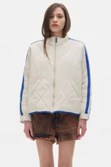Campera acolchada color crema con cierre frontal y cuello alto. Presenta dos franjas azules en las mangas y ribete azul en el cuello y ruedo.