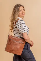 Cartera tipo bandolera de tamaño mediano confeccionada en símil cuero color marrón. Presenta una correa larga regulable, dos compartimientos principales y un bolsillo frontal con cierre de cremallera.