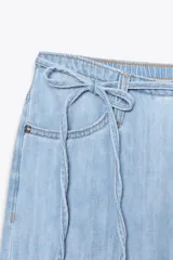 Pantalón denim celeste de tiro medio con cintura ajustable con cordones, bolsillos laterales y de plastrón en espalda. Cierre frontal con cremallera y gancho metálico.