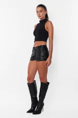 Short negro de cuerina, tiro medio, con bolsillos laterales y traseros, presillas en la cintura y botón metálico.