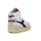 Zapatilla urbana Diadora Heritage de caña alta, color blanco con detalles en azul y beige. Presenta un efecto envejecido en la suela de goma color crema y un gráfico en blanco y negro en la lengüeta.