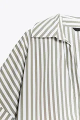 Camisa oversize a rayas verticales color verde y blanco, de cuello solapa y escote pico, con mangas anchas 3/4 terminadas en vuelta y bajo asimétrico.