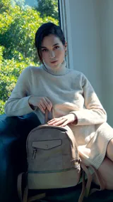 Mochila gris de símil cuero con bolsillo frontal con cierre y broche. Tiene apertura superior, cierres con tiradores en el mismo tono, bolsillos internos, correas regulables con hebilla y asa de mano.