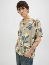 Camisa de manga corta con estampado de hojas en tonos beige, azul y marrón. Tiene cuello resort, cierre con botones y corte relajado.