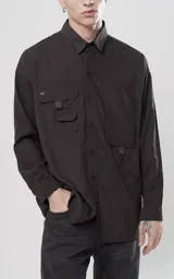 Camisa negra de manga larga, estilo técnica con múltiples bolsillos delanteros y un bolsillo en la parte inferior de la espalda, botones en cartera y mangas, calce oversize, confeccionada en textil ligero suave al tacto.