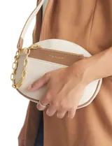 Cartera tipo bandolera de eco cuero con silueta de media luna, color beige y detalles en marrón claro. Incluye un monedero/tarjetero independiente en el bolsillo frontal y una cadena decorativa de eslabones dorados.