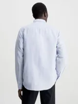 Camisa celeste de lino y algodón, de corte regular, manga larga, cuello en punta, cierre de botones oculto y bolsillo de parche en el pecho con monograma de Calvin Klein en la misma gama de tonos.
