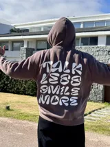 Canguro marrón con capucha y estampado blanco en la espalda con la frase "Talk Less Smile More".