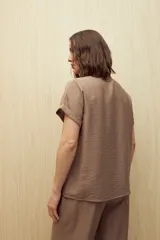 Camisa color marrón claro, de manga corta con puños arremangados, cuello clásico y cierre frontal con botones.