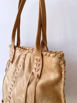 Bolso tipo tote de cuero color camel, con costuras a la vista y tiras de ajuste laterales.