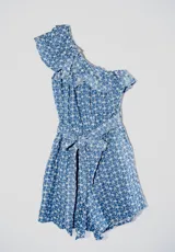 Mono corto azul con estampado de flores blancas, un hombro descubierto con volantes y cintura elástica.