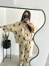 Pijama de dos piezas color beige con estampado de tigres negros y ribetes negros. Incluye camisa de manga larga con cuello y botones, y pantalón largo de corte recto.