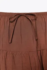 Falda larga color marrón chocolate, de tiro medio con cintura elástica ajustable con lazada y bajo acabado en paneles.