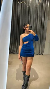 Vestido corto azul brillante de lurex, con un hombro descubierto, manga larga y abertura en la cintura.