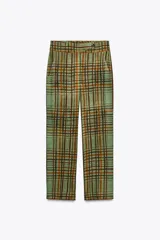 Pantalón de tiro medio con estampado de cuadros color verde y marrón, confeccionado en hilatura de viscosa. Tiene bolsillos delanteros, corte crop y bajo acampanado. Cierre frontal con cremallera y botón.