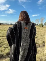 Ruana tejida a mano en telar, confeccionada en lana Merino color negro con detalles en blanco y flecos blancos.