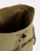 Mochila color beige con detalles en negro. Tiene solapa con tira de ajuste y broche, correas regulables, manija superior, bolsillo frontal con cierre y puller de cordón y goma, bolsillos laterales con cierres y pullers de cordón y goma, y tag de goma.