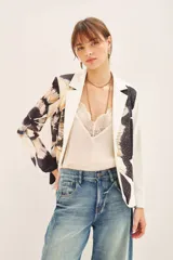 Blazer con estampado abstracto en tonos beige, negro y blanco. Tiene solapas blancas y está adornado con tachas termofijadas en el frente. Se cierra con un cinturón negro con una flor grande.