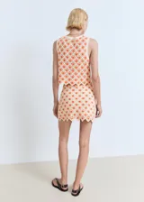 Top de crochet color crudo con flores naranjas, sin mangas, con escote en V y cierre frontal con lazos.