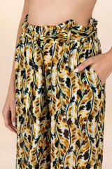 Pantalón largo de tejido ligero y traslúcido con estampado de hojas en tonos mostaza, marrón y negro. Presenta cintura elástica con lazo ajustable y corte recto.