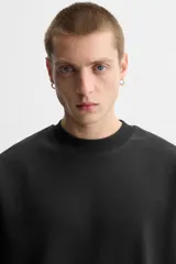 Sudadera negra de corte relaxed fit, confeccionada en tejido interlock de algodón con elasticidad. Tiene cuello redondo, manga corta y bajo acabado en rib.