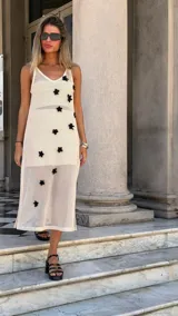 Vestido largo de tejido de red blanco, con apliques de flores negras en relieve. Lleva tirantes finos y tiene un corte recto con abertura lateral. Se usa sobre una prenda interior blanca.