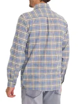 Camisa de franela a cuadros azul, beige y negro, de manga larga con puños abotonados, cuello camisero y cierre frontal con botones de madera. Tiene dos bolsillos de parche con botón en el pecho. Confeccionada en algodón orgánico cepillado.