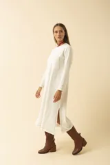 Vestido midi blanco de manga larga, con cuello redondo, bolsillo en el pecho y costuras a la vista.