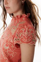 Blusa color coral o terracota con bordado calado floral en tono beige claro. Presenta cuello alto con volado y mangas cortas abullonadas.