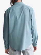 Camisa celeste de manga larga con cuello clásico, cierre frontal con botones, bolsillo de parche en el pecho y logo de Calvin Klein bordado en el bolsillo.
