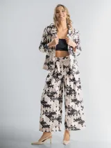 Conjunto de blazer y pantalón elastizado, confeccionado en algodón con lycra y estampa floral en tonos beige, negro y blanco. El pantalón es de corte palazzo y el blazer incluye un aplique floral desmontable.