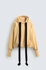 Sudadera color amarillo pálido con capucha ajustable con cordones negros, corte holgado, mangas largas con puños acanalados, bajo abullonado y bolsillo tipo canguro. Edición especial Harry Lambert for Zara x Disney.