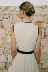Vestido midi de lino color beige, con escote cruzado en pico y sin mangas. Presenta vivos a contraste en negro y cinturón con hebilla forrada. Cierre frontal con botones.