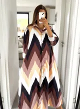 Vestido camisero largo con estampado de chevrón en tonos chocolate, beige, negro y crudo, con cuello camisero y cierre frontal con botones. Mangas largas con puños abotonados.