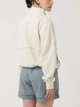 Buzo color beige con cierre frontal parcial y cuello alto. Presenta un bolsillo tipo canguro con diseño tejido a rayas horizontales en tonos marrón, beige y blanco.