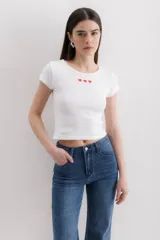 Remera blanca de algodón con cuello redondo y tres corazones rojos bordados en el pecho.