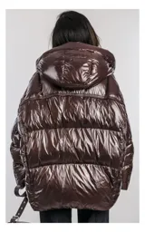 Campera oversize color blanco, confeccionada en nailon suave con un leve brillo. Cuenta con capucha, bolsillos laterales con cremallera, relleno natural y ajuste inferior con cordón. Presenta cierre frontal con cremallera de doble cursor y diseño acolchado.