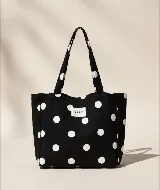 Bolso tipo tote bag de algodón, color negro con estampado de lunares blancos. Posee dos asas de mano y una etiqueta blanca con el texto "AIRE" en el frente.