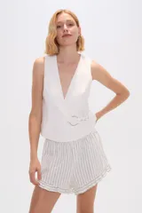 Chaleco blanco sin mangas con escote en V cruzado y ajuste con hebilla metálica.