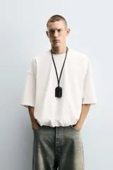 Camiseta blanca de algodón, corte holgado, cuello redondo, manga corta y bajo con elástico interior.